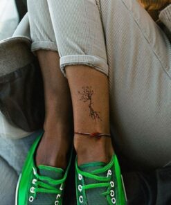 jambe croisés femme avec chaussure verte, elle a un tatouage sur la cheville arbre de vie